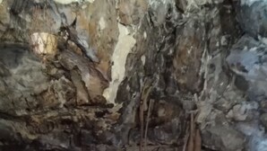 A room with a stone wall, a wooden bench, and a small white device on the floor. - Grotta Paradiso (Modica)
