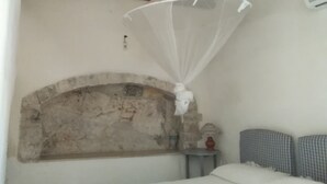 A bedroom with a stone arch, a bed, a bedside table with a lamp, and a hanging mosquito net. - Grotta Paradiso (Modica)