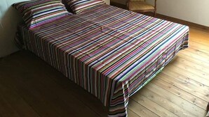 Un letto con copriletto e cuscini a righe, un pavimento in legno e una sedia nell'angolo.