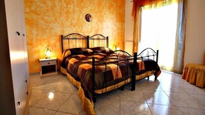 A bedroom with a bed, nightstands, and a window with curtains. - Villa Choco (Modica)