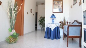 A hallway with a wooden door, a table with a blue tablecloth, a chair, and a lamp. - Villa Choco (Modica)