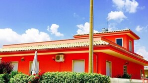 A red building with a tiled roof, a small balcony, and a white fence. - Villa Choco (Modica)