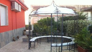 A covered outdoor seating area with a curved bench and a gazebo. - Villa Choco (Modica)