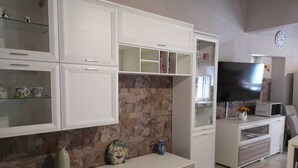 A living room with white cabinetry, a stone wall, a flat-screen TV, and a microwave. - La casa di Viola (Modica)