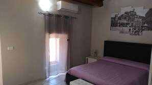 A bedroom with a bed, a nightstand, a window with curtains, and a wall-mounted air conditioner. - La casa di Viola (Modica)
