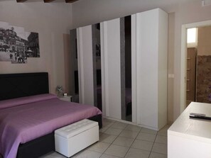 Um quarto com cama, guarda-roupa, escrivaninha e espelho.