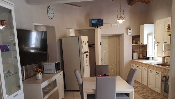 A compact kitchen with a dining area, a TV mounted on the wall, and a refrigerator. - La casa di Viola (Modica)