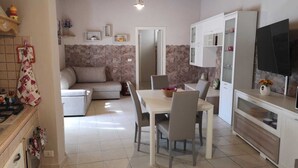 A modern kitchen with a dining area, stone wall, and a TV mounted on the wall. - La casa di Viola (Modica)