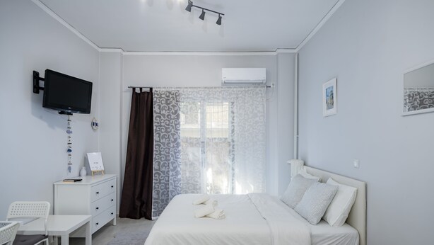 A modern bedroom with a bed, a desk, a chair, a TV, and an air conditioning unit. - Beautiful studio at Panathenaic Stadium (Athens)