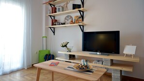 Una sala de estar con una televisión de pantalla plana, estanterías de madera, una maleta verde y una mesa con un tazón de bocadillos.
