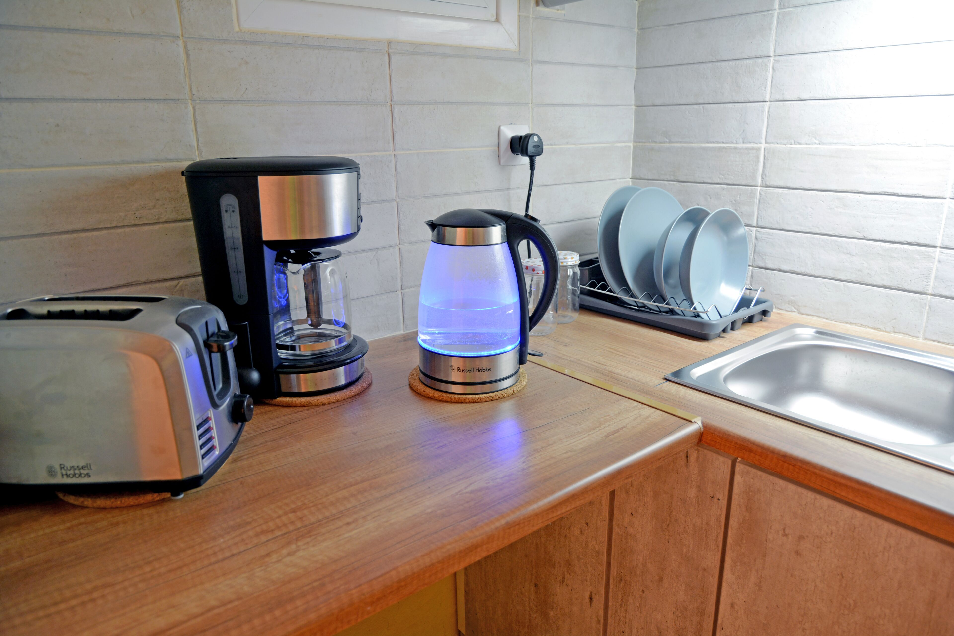 A kitchen with a coffee maker, a kettle, and a dish rack.