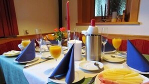 Una mesa de comedor preparada con platos, cubiertos, vasos y una jarra de jugo de naranja.