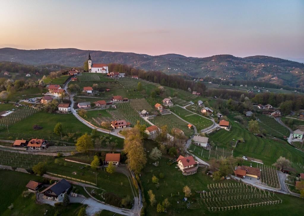 An aerial view of a village with a prominent church, winding roads, and agricultural fields.