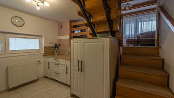 A kitchen with white cabinets, a wooden staircase, and a window with blinds.