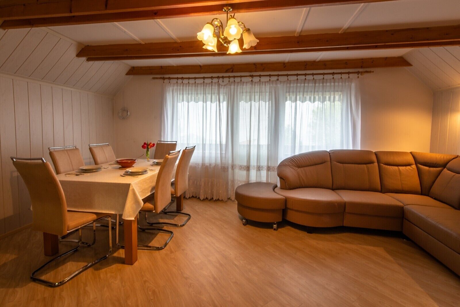 A dining area with a table set for four, a brown leather sofa, and a wooden ceiling with exposed beams.
