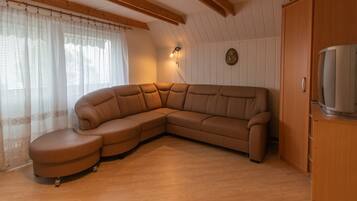Un sofá seccional en forma de L con chaise, un aparador de madera y un televisor sobre un mueble bajo.