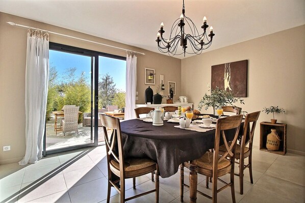A dining area with a table set for breakfast, a chandelier, and a view through a sliding glass door.