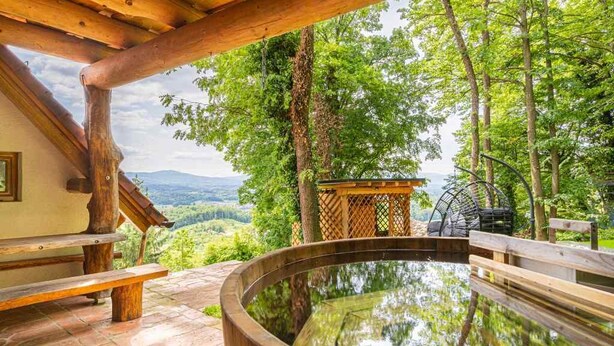Una terraza de madera con un jacuzzi, bancos y vistas a un valle boscoso.
