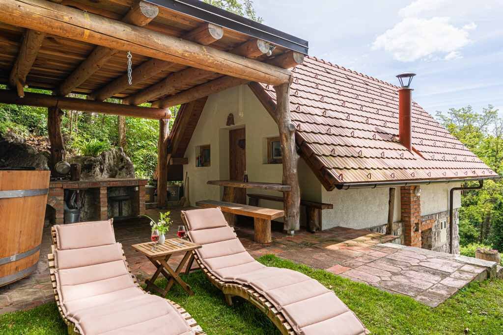 Un espace extérieur rustique aménagé avec des fauteuils confortables et une table en bois, une cheminée en pierre et un patio couvert.