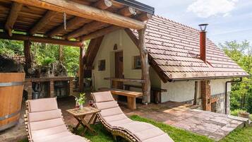 Un espace extérieur rustique aménagé avec des fauteuils confortables et une table en bois, une cheminée en pierre et un patio couvert.