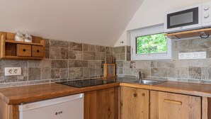 Una cocina con protector de piedra, armarios de madera, microondas integrado y ventana con vista a la vegetación.