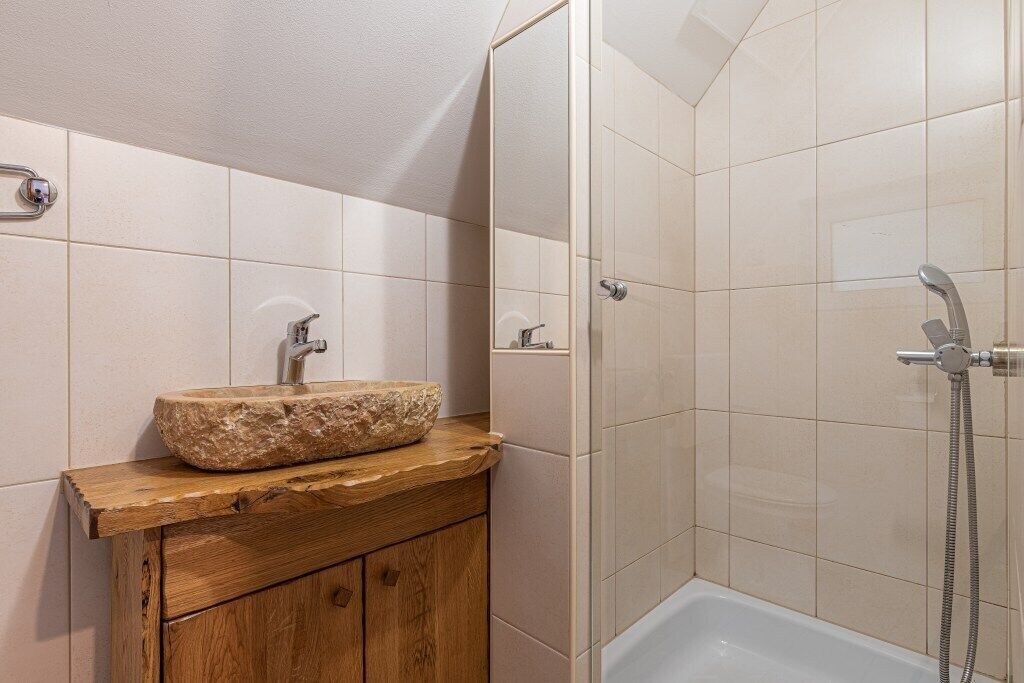 A bathroom with a stone sink, wooden vanity, and a walk-in shower.