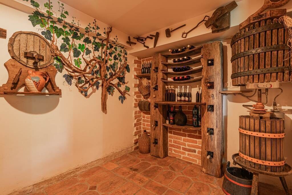A rustic wine cellar with wooden shelves, barrels, and a wall-mounted grapevine decoration.
