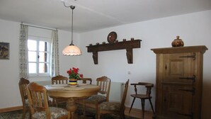 Un comedor con una mesa redonda de madera, seis sillas, una lámpara colgante, un aparador de madera y una ventana con cortinas.