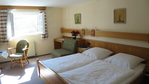 Una habitación de hotel con dos camas individuales, un cabecero de madera, un escritorio pequeño, una silla y un radiador.