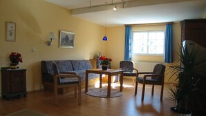 Una sala de estar con un sofá, dos sillas, una mesa de centro, una lámpara, una planta en maceta y una ventana con cortinas.