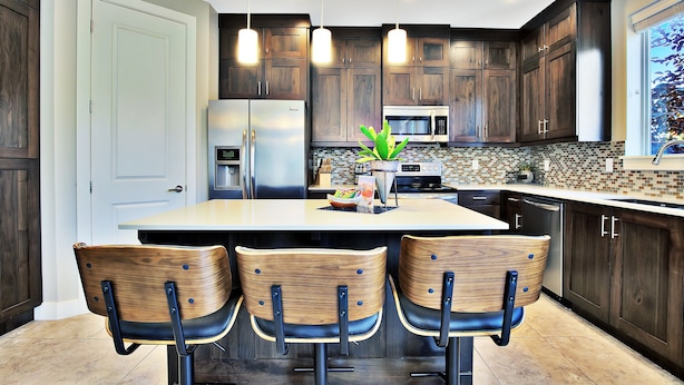 A modern kitchen with dark wood cabinets, a central island with bar stools, a refrigerator, microwave, and a dishwasher.