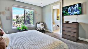 A bedroom with a bed, a dresser, a TV, and a window with a view of trees and mountains.