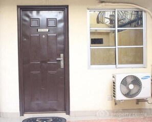 A dark brown door with a sign above it, a window with multiple panes, and an air conditioning unit mounted on the wall. - Tobby Royal Suites (Lagos)