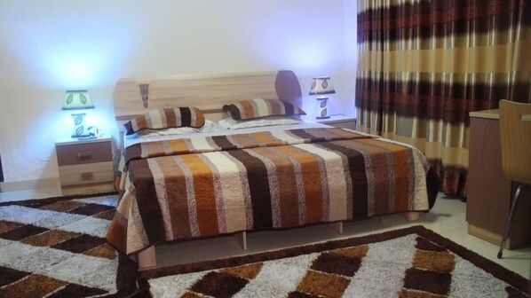 A bedroom with a bed, nightstands, a desk, and a chair. - Tobby Royal Suites (Lagos)