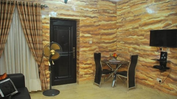 Een woonkamer met een behang, een zwarte deur, een ventilator, een televisie en een eethoek met stoelen en een tafel.