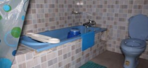 A bathroom with a blue bathtub, a white toilet, and a tiled wall. - Tobby Royal Suites (Lagos)