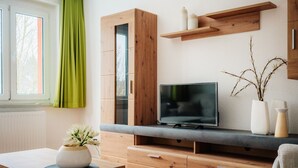 A modern living room with a wooden cabinet, a flat-screen TV, and a dining area with a table and chairs. - Bode-Apartments (Oberharz am Brocken)