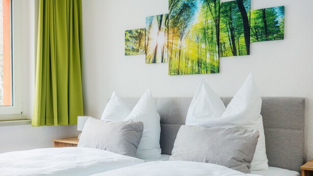 A neatly made bed with white bedding, a grey headboard, and multiple pillows. - Bode-Apartments (Oberharz am Brocken)