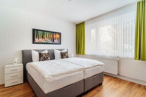 A bedroom with a double bed, a nightstand, a framed picture on the wall, and a window with green curtains. - Bode-Apartments (Oberharz am Brocken)