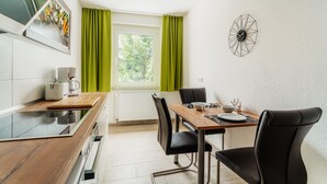 A modern kitchen with a dining table, chairs, and a window with green curtains. - Bode-Apartments (Oberharz am Brocken)