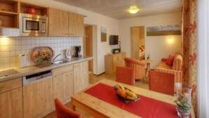 Une cuisine compacte avec des meubles en bois, un four à micro-ondes et un évier. On y trouve également un coin repas avec une table, des chaises et un panier de fruits.