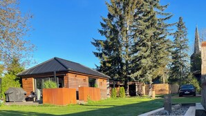 Una cabaña moderna de madera con techo metálico, rodeada por un césped cuidado y una terraza de madera.