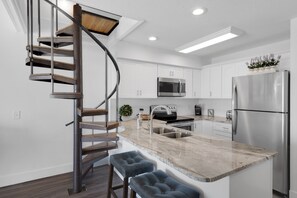 Une cuisine moderne dotée d’un îlot central, d’appareils électroménagers en acier inoxydable et d’un escalier en colimaçon.