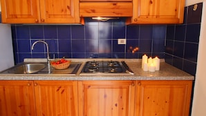 A kitchen with wooden cabinets, a granite countertop, a stainless steel sink, a gas stove, and a basket of tomatoes.