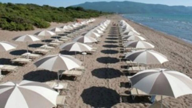 A beach with rows of umbrellas and lounge chairs facing the sea.