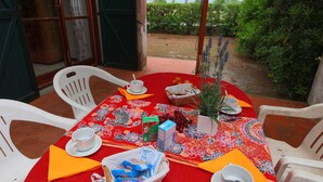 An outdoor dining area with a red tablecloth, white chairs, and a view of the sea.