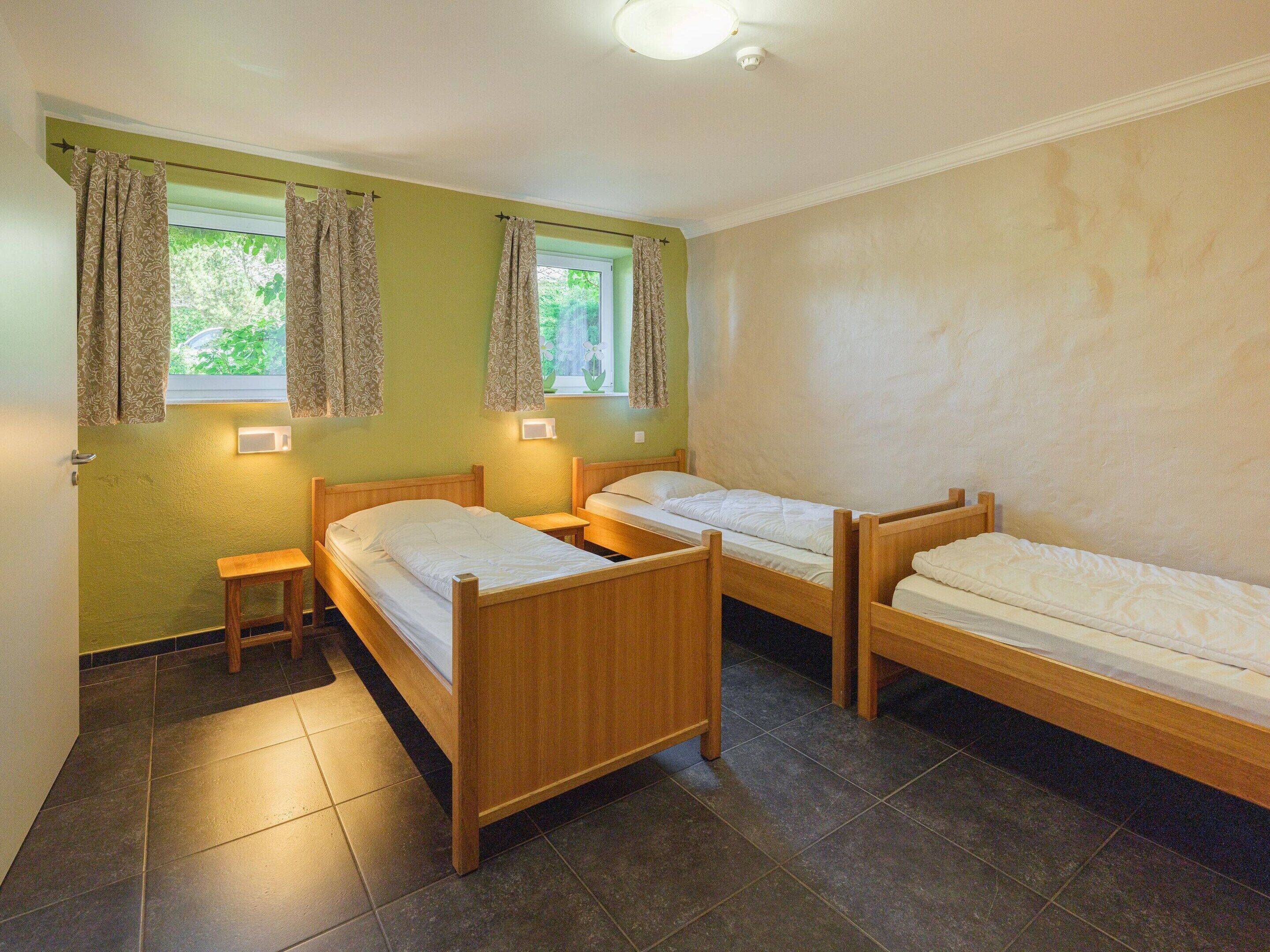 A room with three wooden beds, a small table, and a window with curtains.