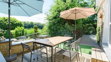 An outdoor patio with a table and chairs, a large umbrella, and a stone wall.