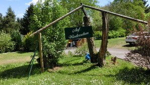 En skylt med texten ”Auf Wiedersehen” placerad i en lantlig miljö med grönska och en parkerad bil.