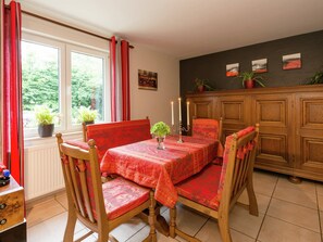 A dining area with a table set for four, wooden chairs, a cabinet, and a window with curtains.